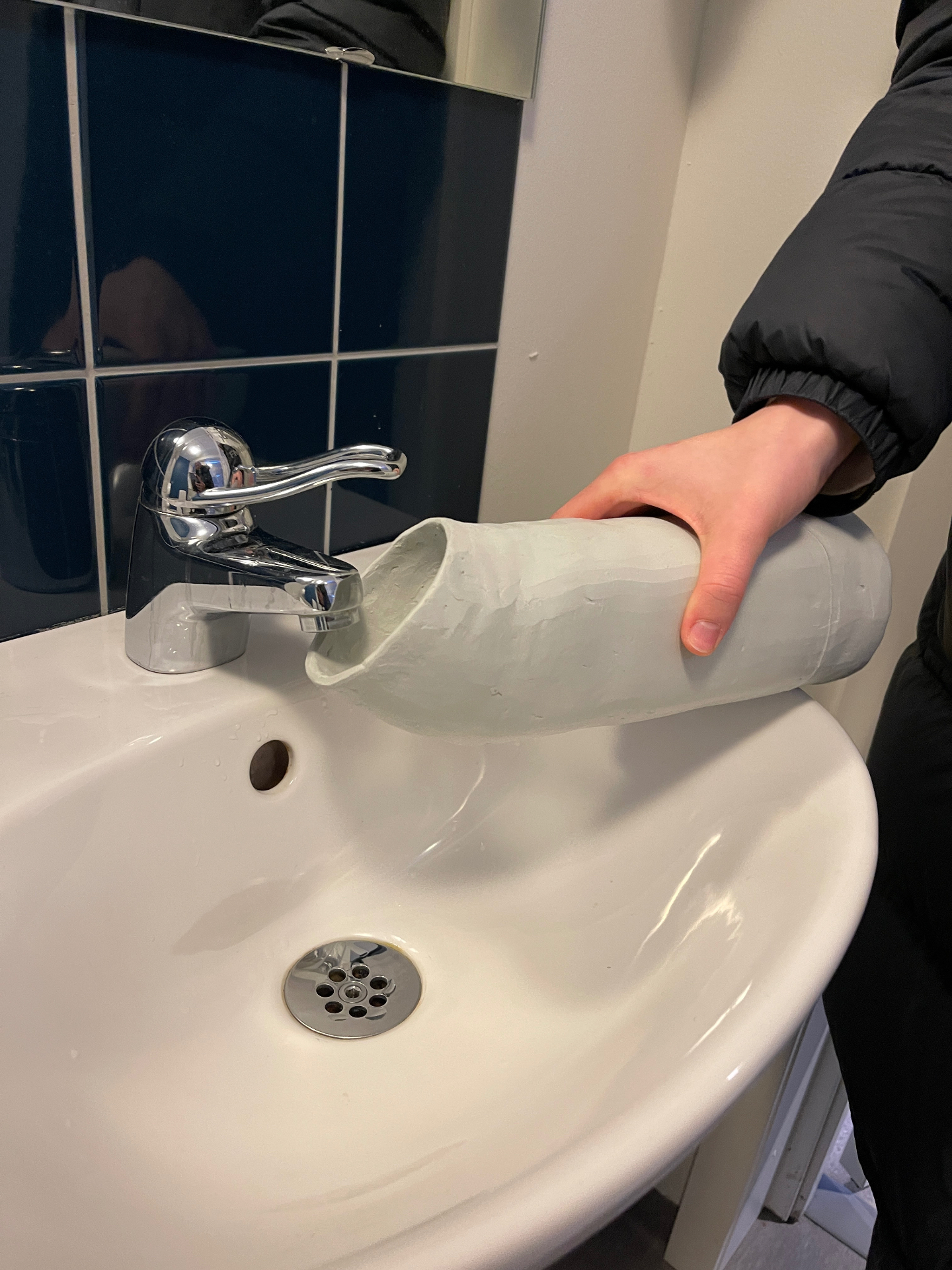 Clay prototype held under a tap over a bathroom sink.