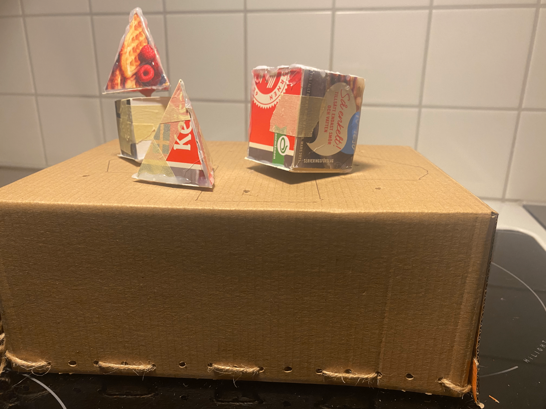 Front view of an early cardboard prototype of the activity box, with small paper pyramids and cubes placed on top.