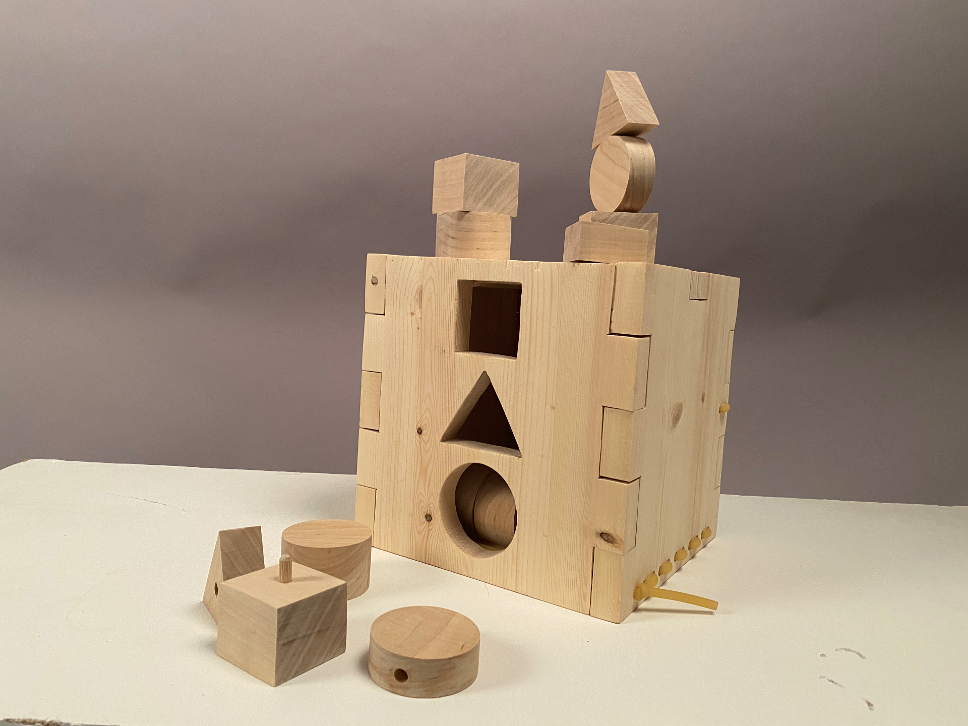 Studio photo of the front of the wooden Activity Box, showing the square, triangle and circular shape sorting openings, the flat building surface on top and two towers of loose wooden blocks stacked on top of the box.