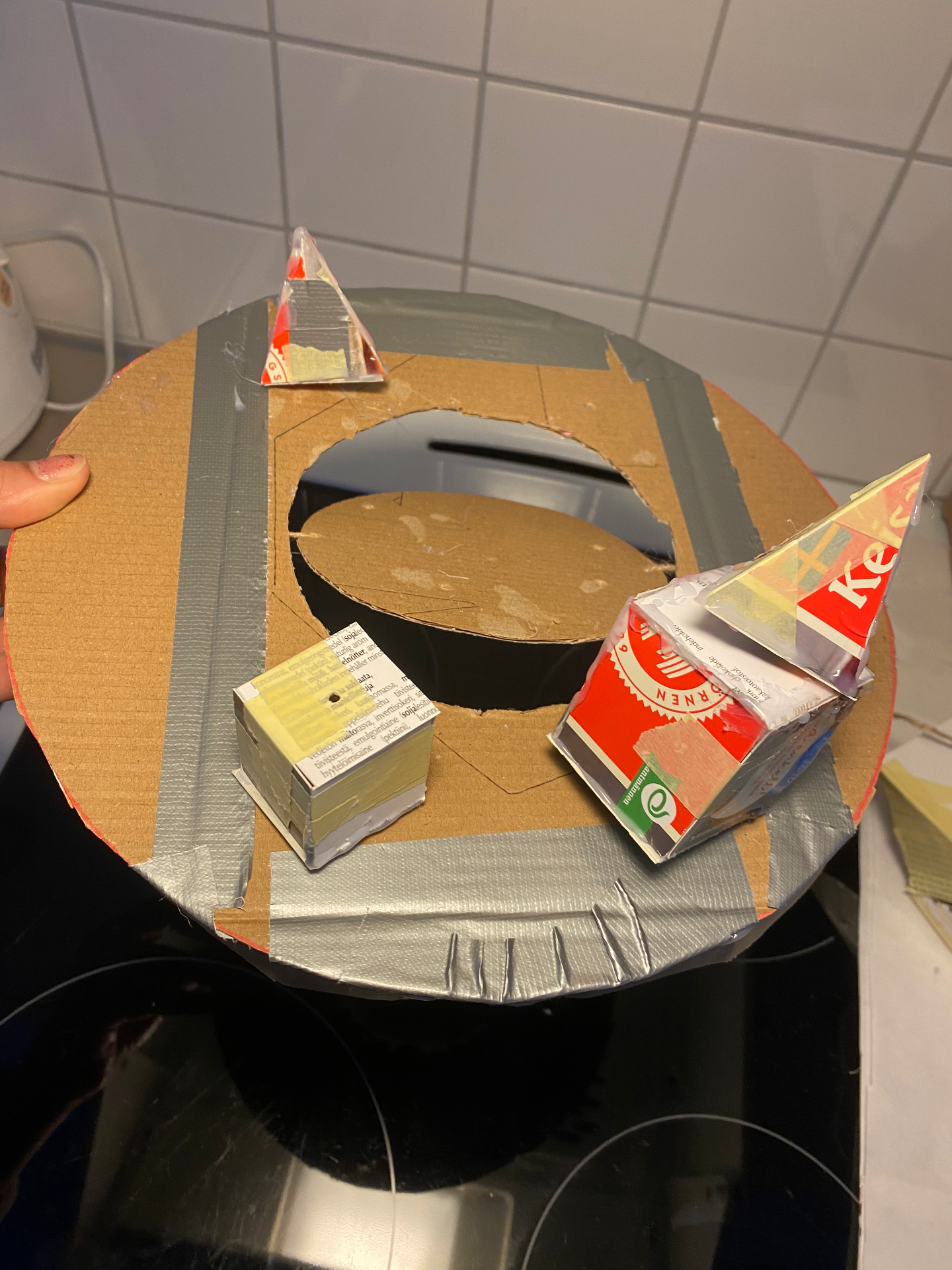 Top view of the cardboard prototype showing a circular opening and loose paper shapes.