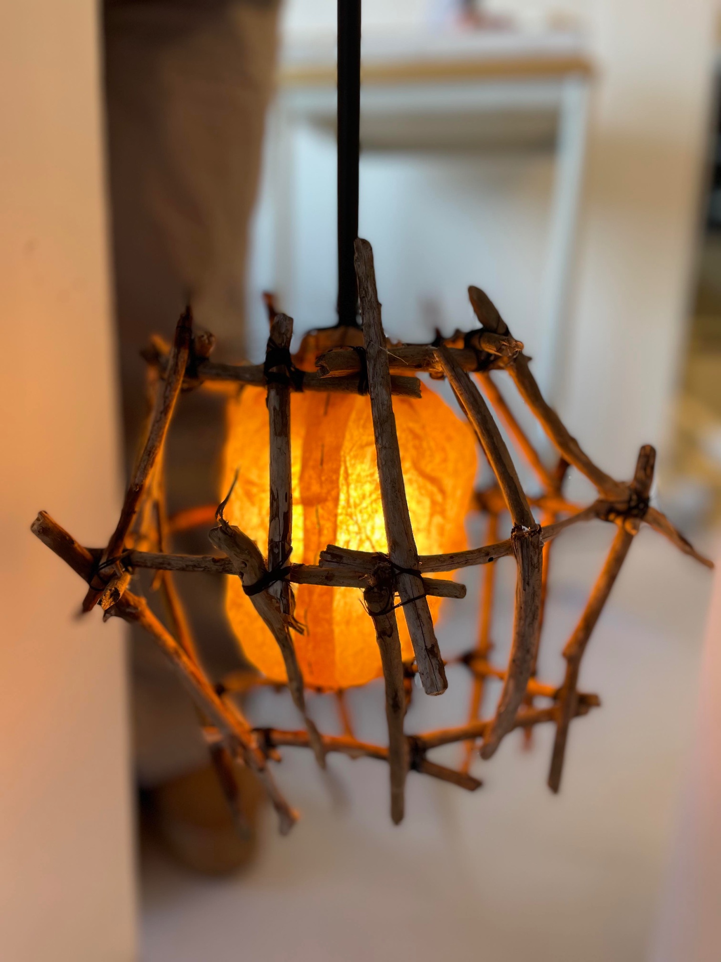 Close up of the illuminated lamp showing branches tied with string and warm light glowing through paper.