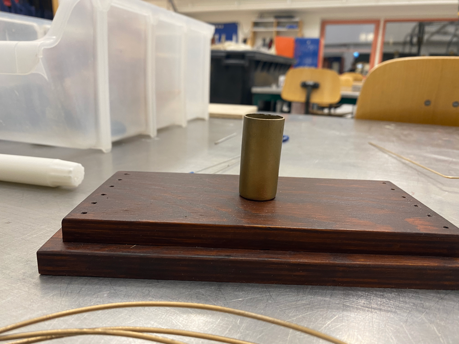Stained stepped plywood base with a small brass coloured candle holder positioned in the centre, photographed in the workshop.