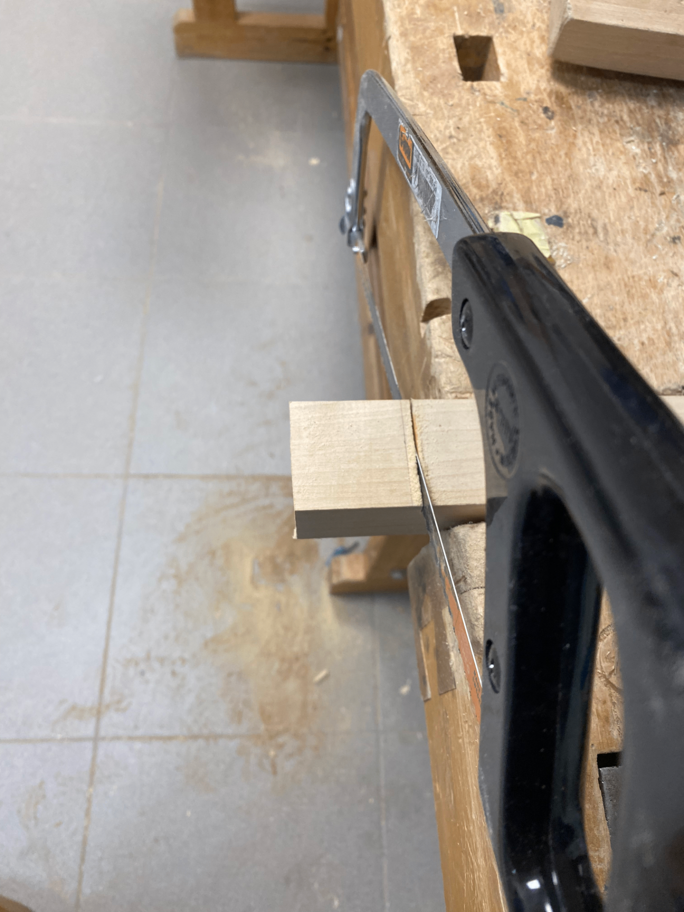 Handsaw cutting a small wooden block clamped to a workbench in the workshop.