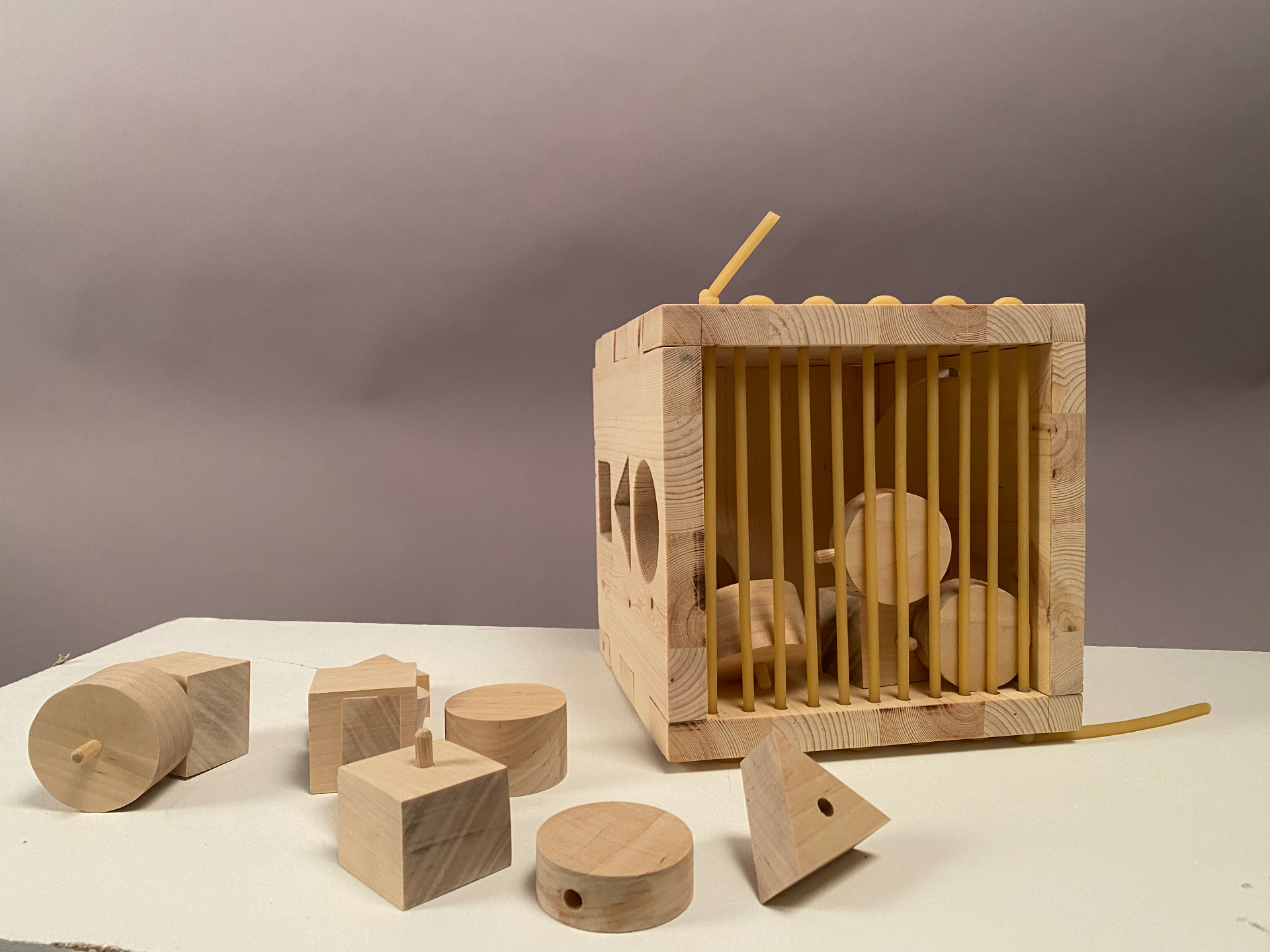 Studio photo of the wooden Activity Box seen from the rubber band side, with vertical rubber bands stretched across a wide opening and loose wooden pieces visible inside the box behind them.