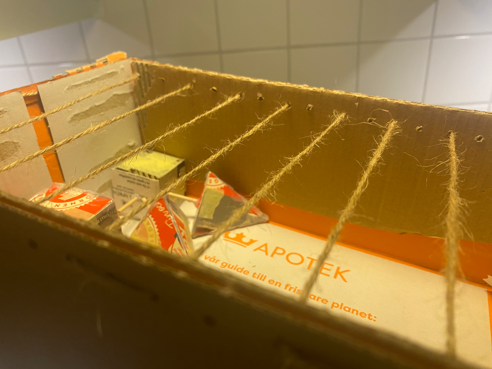 Inside view of a cardboard prototype with strings stretched across the top and loose paper pieces held below.
