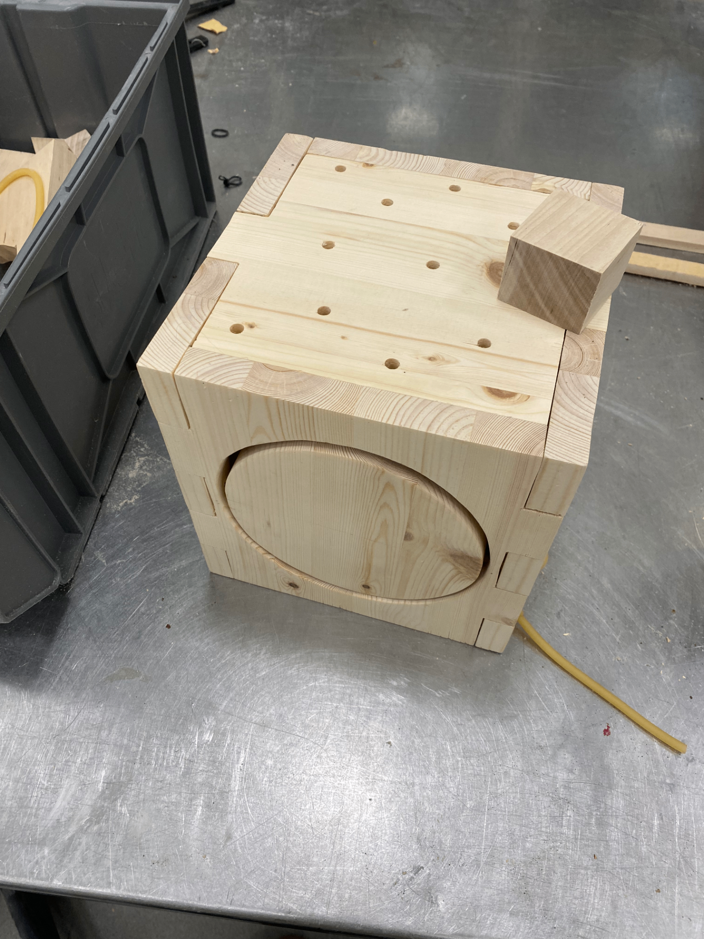 Wooden activity box during construction on a metal workbench, with visible wooden joints on the top surface.